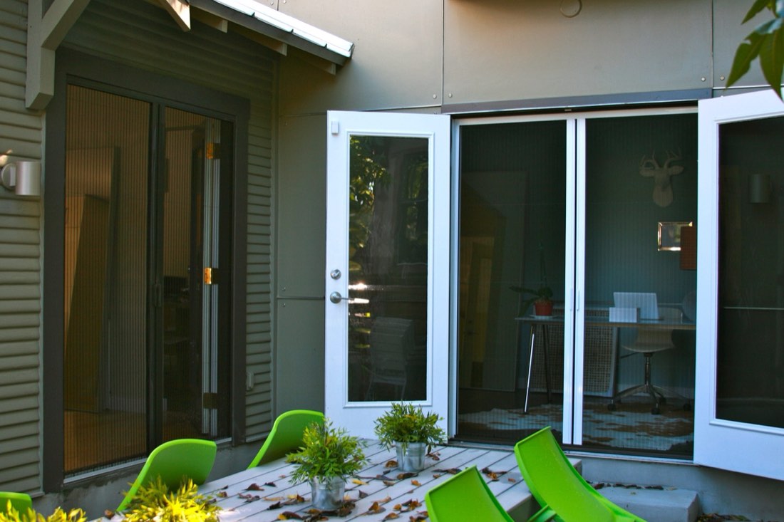 Two sets of French doors with pleated screens opening onto a patio with green chairs